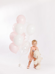 Little cute girl holds branch of balloons and large Teddy bear enjoy festive birthday event wear pink pastel summer dress isolated on a white background.