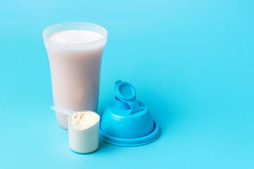 Protein shake and a scoop on blue background, copy space.