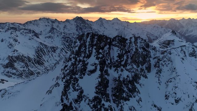Aerial around epic rocky peaks slope alpine high mountains natural epic landscape. Snow covered tops mountain chain. Picturesque orange beautiful dawn. Caucasus Russia unique nature. Freedom of peace