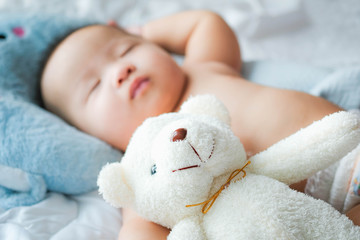 top view Portrait of a newborn Asian cute baby boy wore blue Infant bodysuit on the bed , Charming Fat baby 5 month old lies in bed with a doll,enjoy and happy