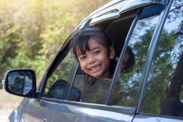 Little girl enjoying the trip smile and show head out of car window on the road.