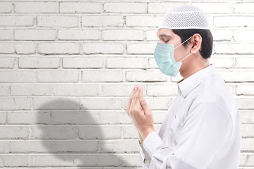 Asian Muslim man wearing flu mask standing while raised hands and praying