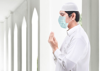 Asian Muslim man wearing flu mask standing while raised hands and praying