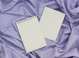 Fototapeta premium empty notebook with sheets on a spring and a cardboard card on a purple striped fabric.