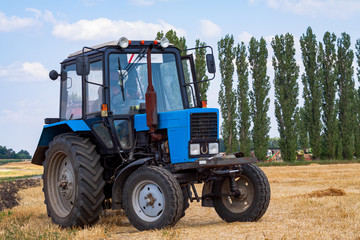 A tractor with a trailed bale making machine collects straw rolls in the field and makes round large bales