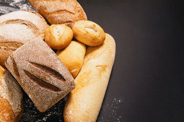 Assortment of fresh baked bread with a golden crust a black rustic background. Flat layout with place for advertisement.