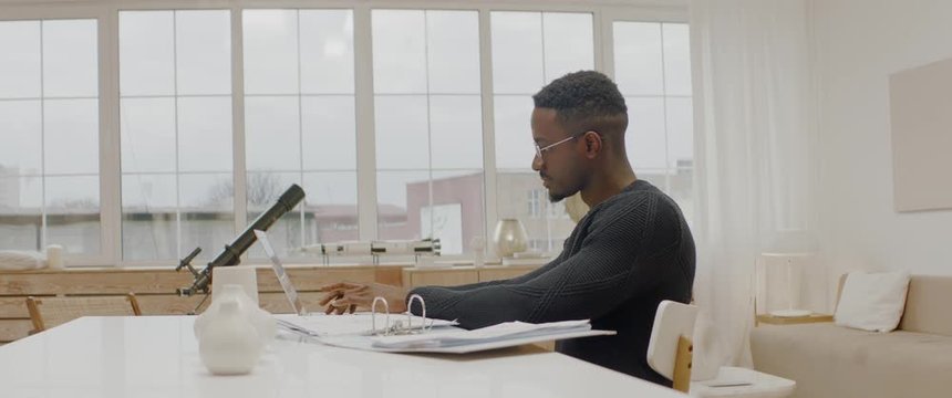 Handsome African American male working from home, using laptop in living room, checking documents. ARRI Alexa Mini, 2x anamorphic lens