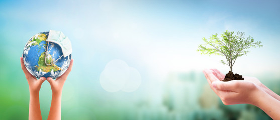 Earth Day concept: hands holding Corona virus or COVID-19 Earth globe wearing a mask  and  tree over  nature background. Elements of this image furnished by NASA