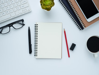 Top view from above of Blank notebook with keyboard, glasses and coffee, phone on white table background. Workplace for creative work of designer. Flat lay, Business-finance concept with copy space.