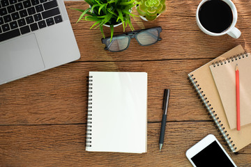 Top view from above of Blank notebook with laptop, glasses and coffee on wood table background. Workplace for creative work of designer at home. Flat lay, Business-finance concept with copy space.