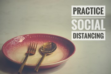 Conceptual still life photo of empty plate with cutlery with the message promoting social distancing, self isolation and home quarantine to prevent the spread of covid-19 pandemic