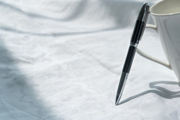 part of white ceramic coffee cup with metal luxury pen on fabric in work from home concept