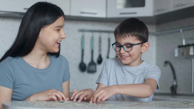 Cheerful Boy and girl will put together a puzzle while sitting at a table at home in the kitchen. Close-up