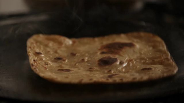 Close up of steaming hot roti cooked on a cast iron pan and flipping with bare hands