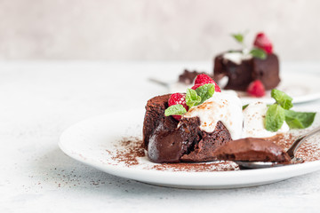 Delicious chocolate fondant or lava cake with cream, raspberries and cream, light grey concrete background. Hot chocolate dessert (pudding) with liquid center. Fondant au chocolate. 