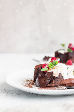 Delicious chocolate fondant or lava cake with cream, raspberries and cream, light grey concrete background. Hot chocolate dessert (pudding) with liquid center. Fondant au chocolate. 