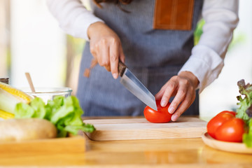 Closeup image of a woman chef cutting and chopping tomato by knife on wooden board