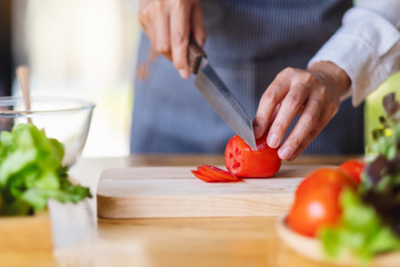 Obraz na płótnie Canvas Closeup image of a woman chef cutting and chopping tomato by knife on wooden board