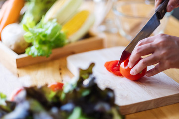 Closeup image of a woman chef cutting and chopping tomato by knife on wooden board