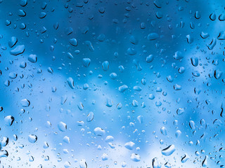 Rain drops on window glasses surface with blue cloudy background .