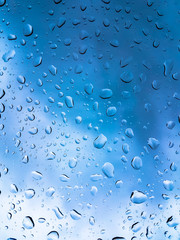 Rain drops on window glasses surface with blue cloudy background .