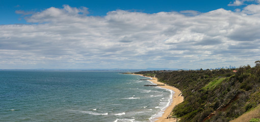 panoramic view of the bay stretching out into the distance with empty sandy beaches and calm waves crashing in with the city of Melbourne skyline in the distance