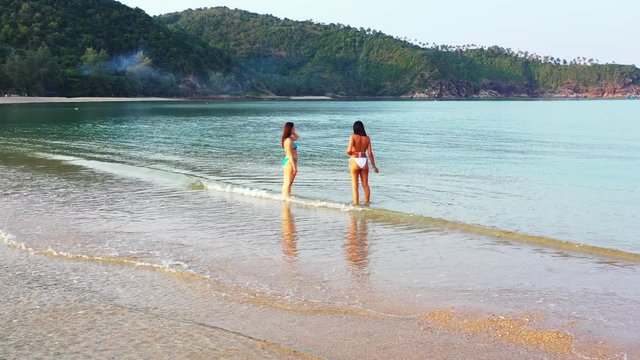 Playful girls in swimsuit washing feet on clear water of shallow lagoon on tropical island with green hills in Vietnam