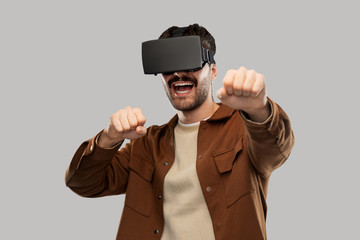 future, technology and people concept - happy smiling young man with mustaches in virtual reality headset or vr glasses over grey background