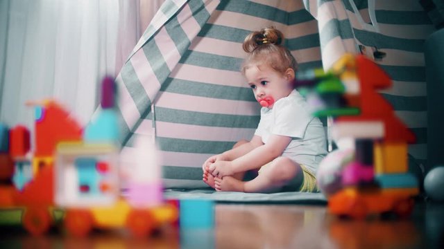 Unhappy frowned baby girl sits in toy teepee tent at home. Self-isolation concept
