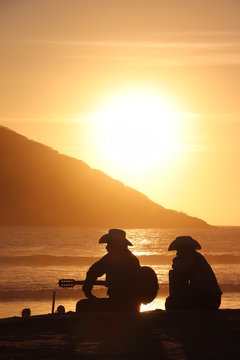 Hombres con guitarra a contraluz durante el atarceder en la playa