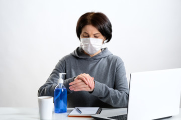 An elderly woman in a protective mask treats her hands with an antibacterial gel

