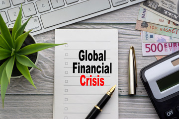 GLOBAL FINANCIAL CRISIS text with notepad, keyboard, decorative vase, fountain pen, calculator and banknotes currency on wooden background. Business and Copy space concept