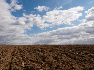 clouds floating in the blue sky over a plowed fertile field in spring