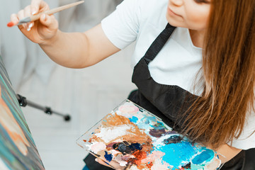 Art, the work of the artist. Young beautiful girl artist paints a picture. Workshop of the artist. The process of creativity. Drawing and paint. Inventory of the artist. Close-up.