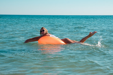 The girl rides lying on an orange rubber ring in the sea, and very joyful