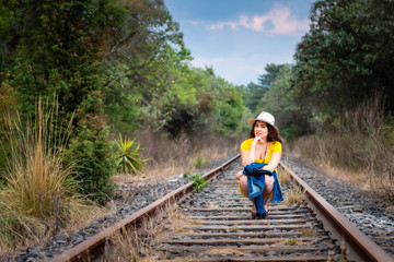 Real woman sitting on the railroad track, in high heels, yellow dress and hat