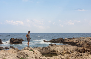 Fototapeta na wymiar Adult man walks on the rocks from the shore of Greece, in summer vacation