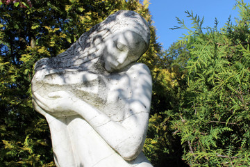 Part of a stone sculpture of a sad woman on a background of trees and sky.