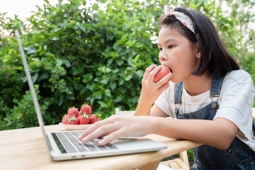 Young girls eating apple and learn about online lessons by laptop in the front yard. She is educated at home because of the epidemic of a new strain of the corona virus, or COVID-19. Stay at home.