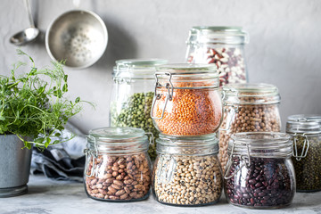 Set of different legumes in glass jars on, concrete white table. A source of protein for vegetarians. The concept of healthy eating and food storage. - obrazy, fototapety, plakaty