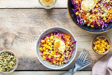 Vegetable salad of fresh red cabbage with carrots, onions, corn, mung seedlings in a plate on wooden background. Selective focus. Top view. Copy space.