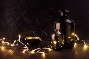 Rich festive home decoration in simple style in black and gold color - warm lights glowing on dark wooden plank with glass vases, black candlestick.