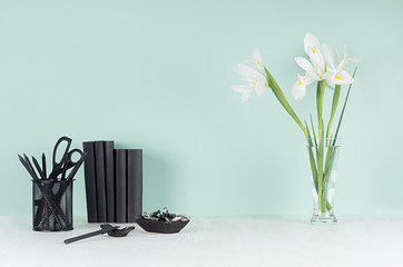 Fresh home workplace with style black stationery, books and  white iris bouquet in glass vase in trendy green mint menthe interior on white wood table, copy space.