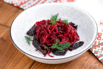 Traditional Ukrainian beetroot salad served in white bowl over rustic wooden table with traditional tablecloth.