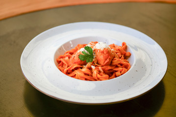 Macaroni pasta with bolognese sauce and parmesan cheese on a white plate on dark rustic wooden table.