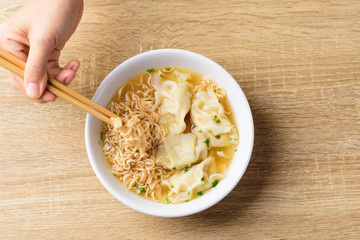 Instant noodles soup and wonton dumpling stuffed with minced pork in a bowl eating by chopsticks, Asian food, Top view