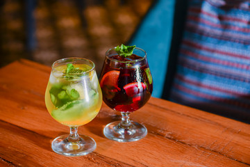 Two colorful refreshing cocktails served on a dark rustic wooden table with blurred background.
