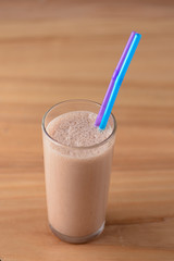 Vanilla chocolate milkshake in a tall galss with two plastic straws on light rustic wooden table.