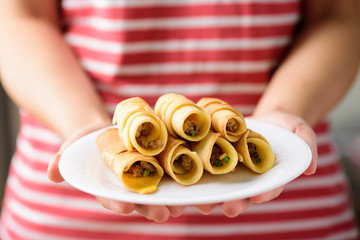 Thai dessert (Khanom Tokyo), pancake roll stuff with minced pork on white plate holding by hand