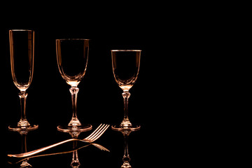 Verres à pied et fourchette sur fond noir avec reflet.	